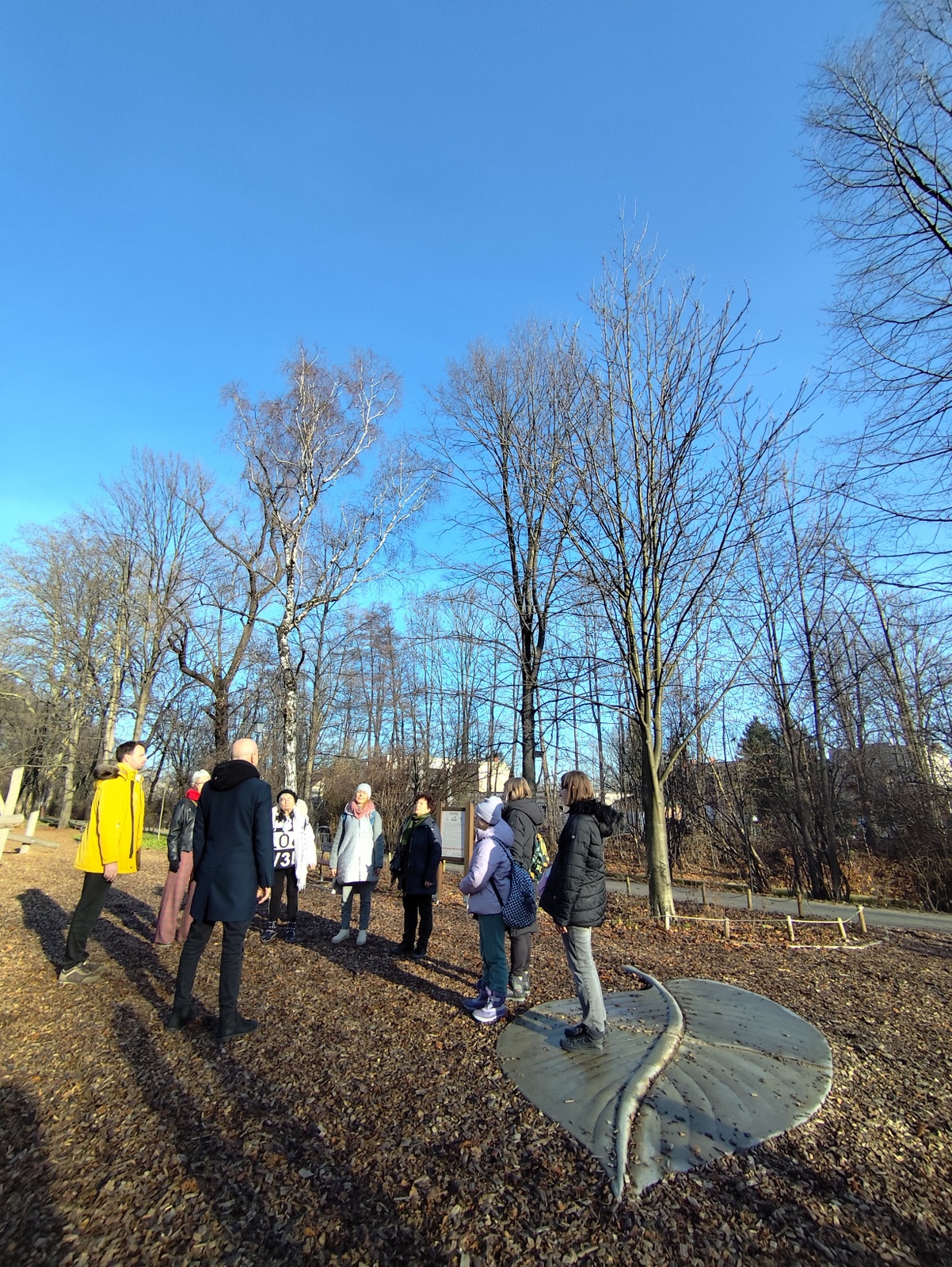 Group of people standing opposite each other with closed eyes during a mindfulness exercise led by a local musician. They are listening to the surrounding nature.