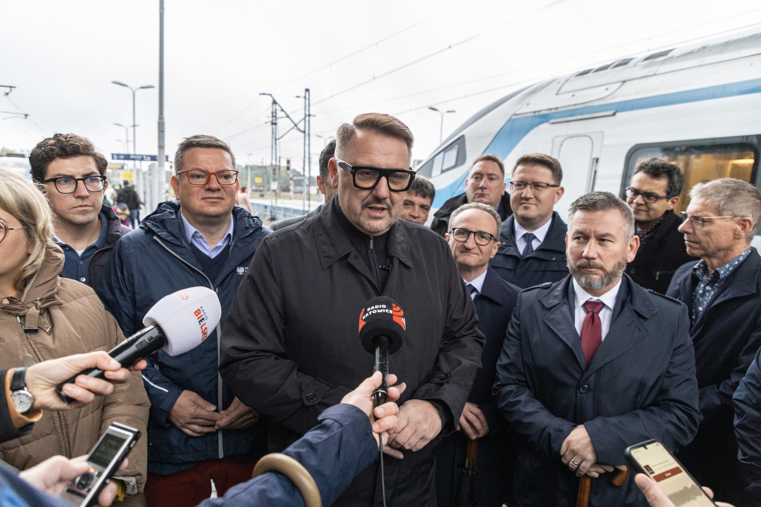 Na zdjęciu stojący ludzie 