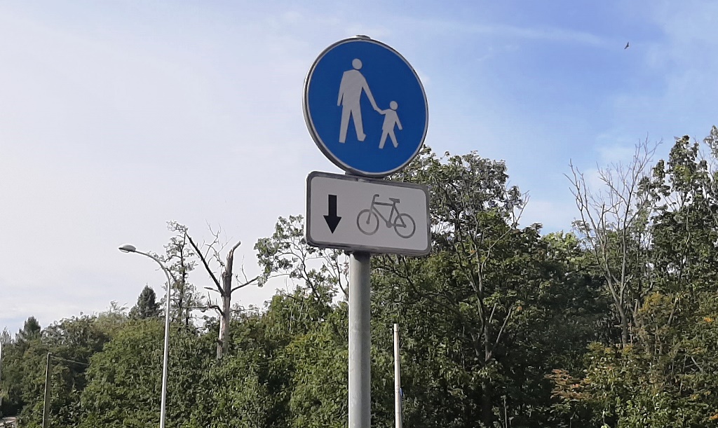 grafika przedstawiająca znak oznaczający drogę dla pieszych i rowerów z jednokierunkowym ruchem rowerowym, gdzie rowerzyści ustępują pieszym  pierwszeństwa; w tle zieleń. 