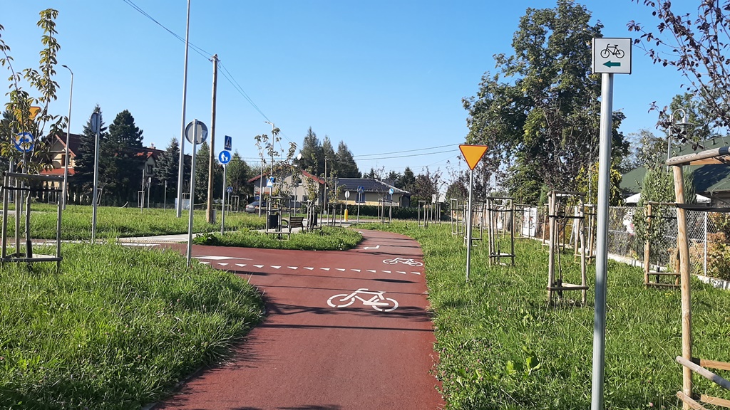 zdjęcie przedstawiające drogę dla rowerów, znaki drogowe, budynki oraz zieleń