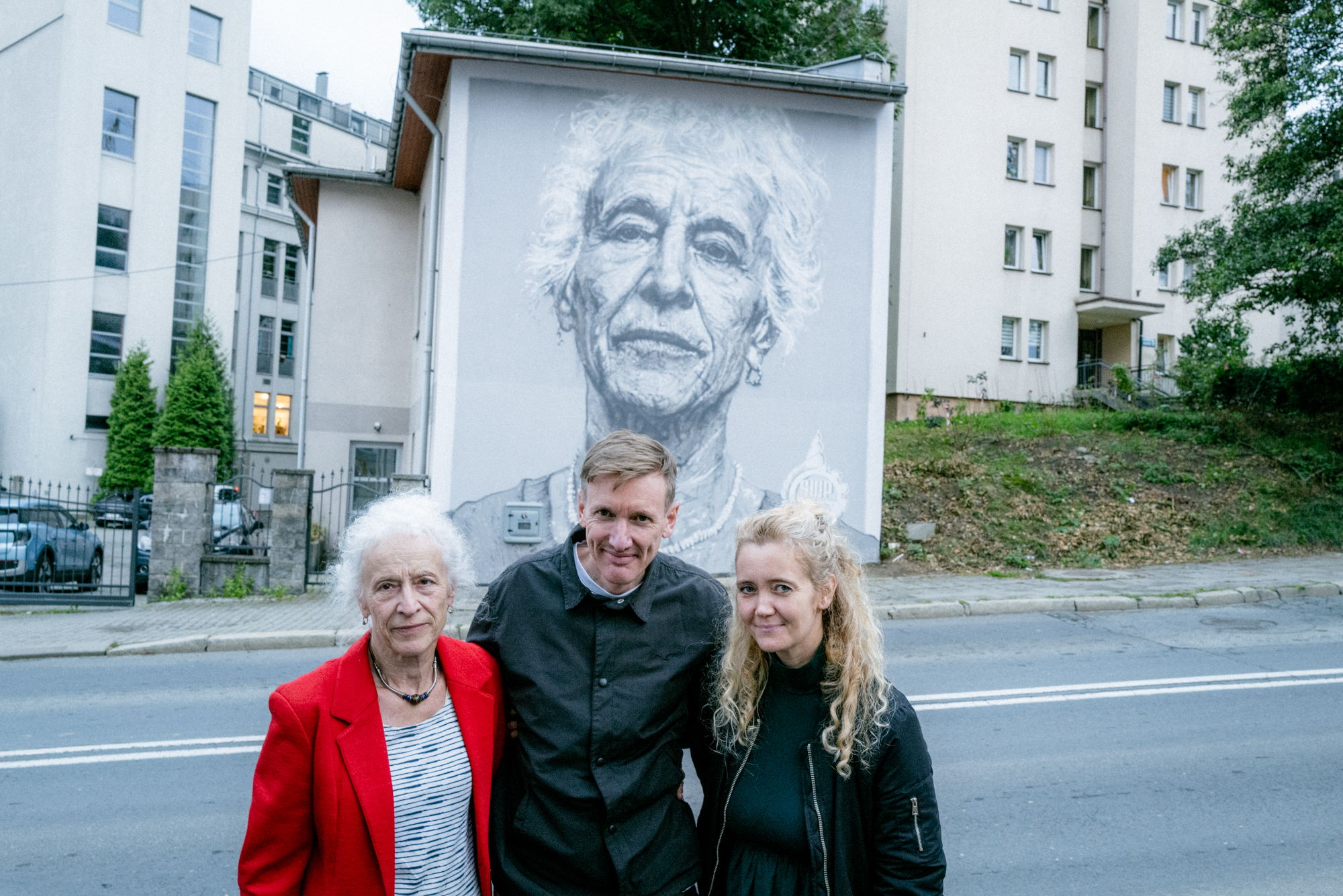 Na zdjęciu twórca, kuratorka projektu i osoba uwieczniona na muralu, w tle mural