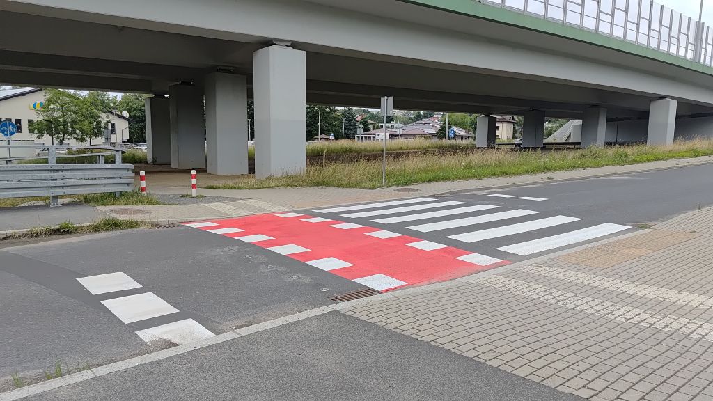 zdjęcie przedstawiające fragment drogi z przejazdem dla rowerów, przejściem dla pieszych, chodnikiem oraz drogą ekspresową w tle 