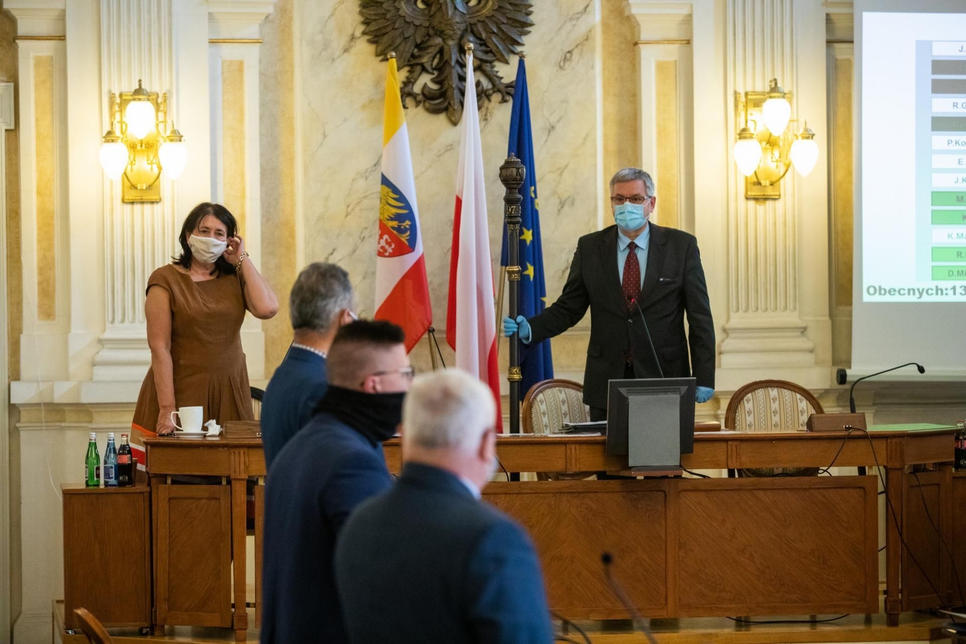 Na zdjęciu stojący ludzie 