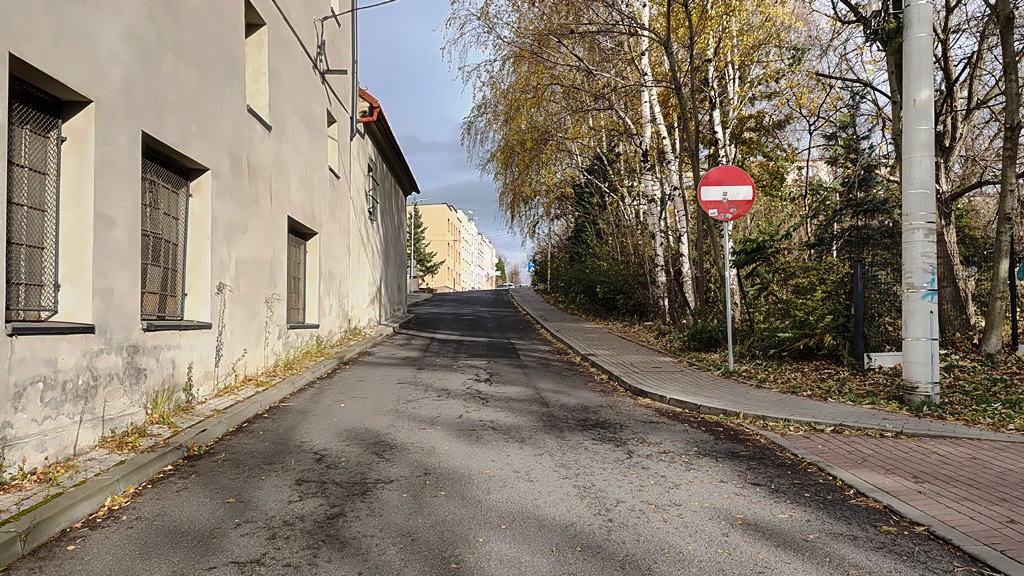 zdjęcie przedstawiające fragment drogi, znak drogowy, budynki oraz zieleń