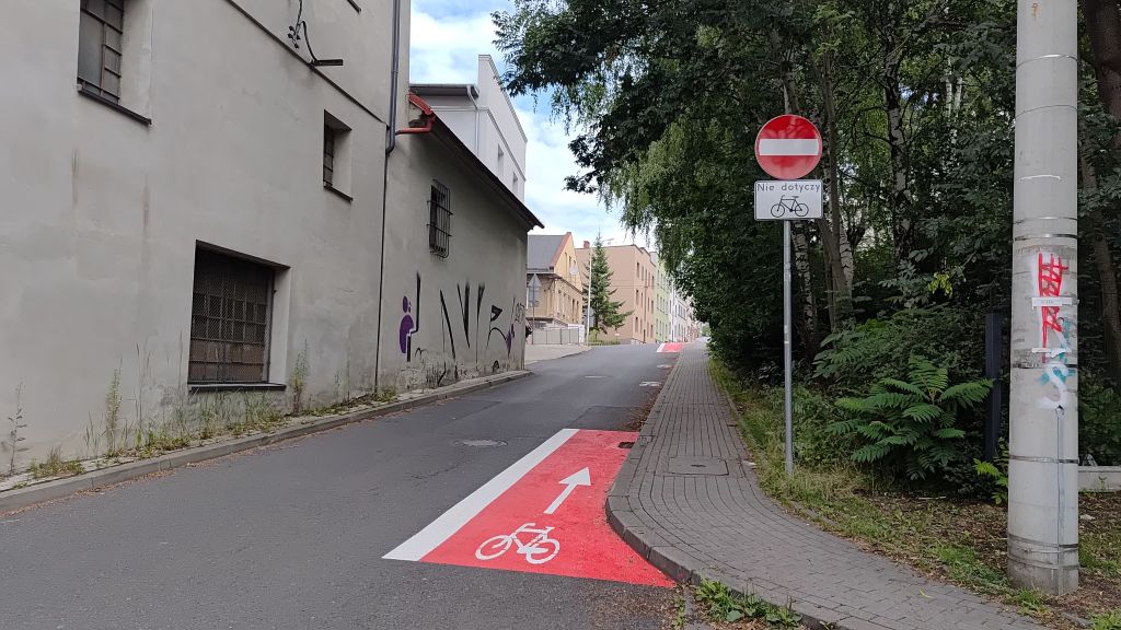 zdjęcie przedstawiające fragment drogi, znak drogowy, budynki oraz zieleń