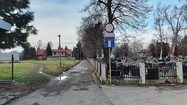 zdjęcie przedstawiające drogę obok cmentarza, znaki drogowe, budynki oraz zieleń