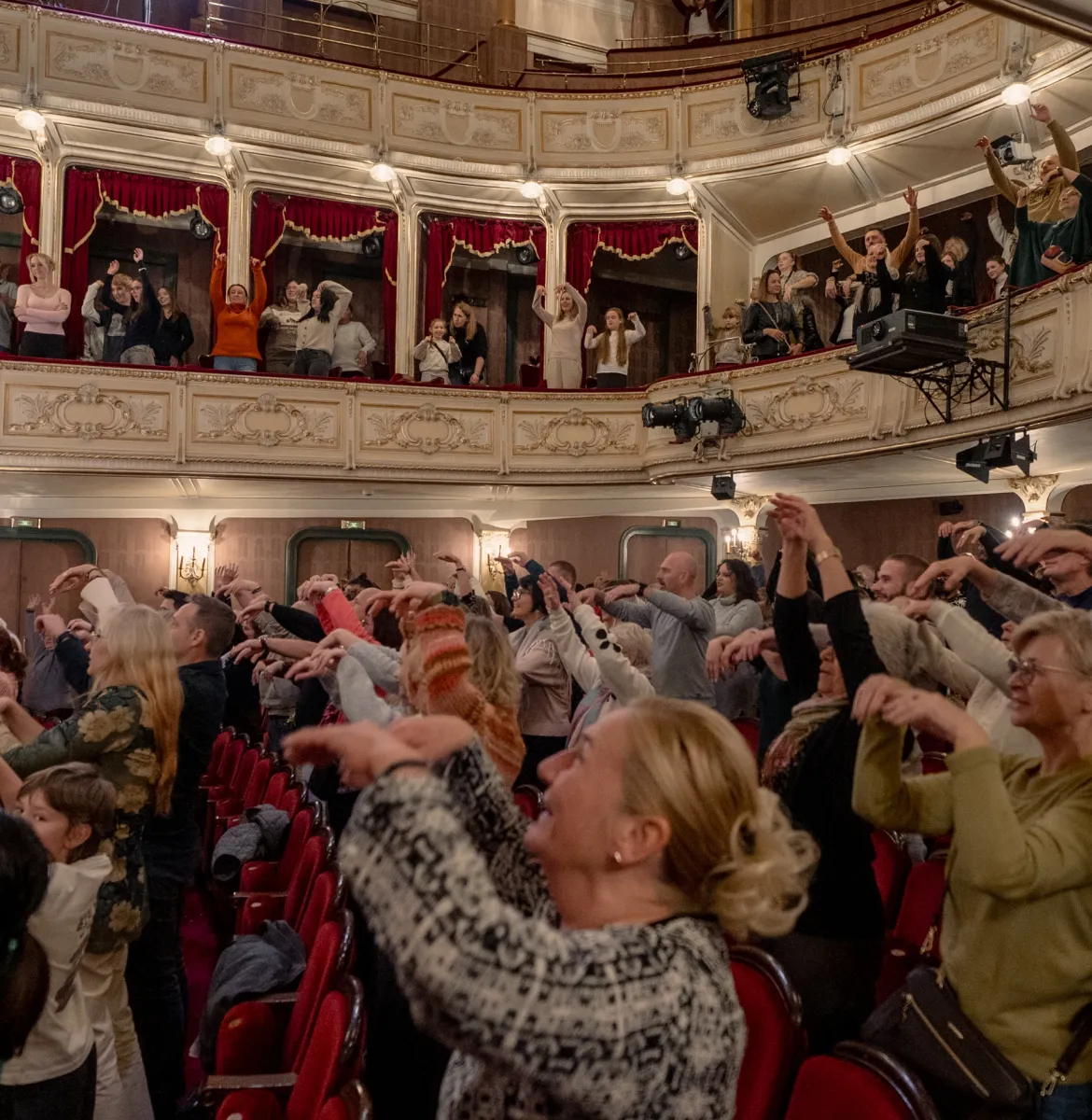 Na zdjęciu osoby na widowni wyrażające aplauz w języku migowym