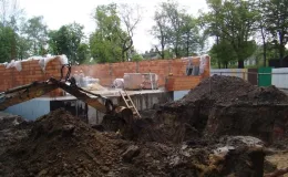 Budowa sali gimnastycznej - na zdjęciu fragment budowy, maszyna budowlana oraz zieleń