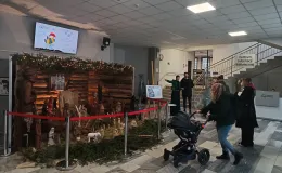 Zdjęcie przedstawiające szopkę bożonarodzeniową i osoby stojące przed nią w budynku.
