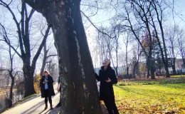 Local musician standing beside a tree with sound-recording equipment and headphones, eyes closed and smiling, listening to sounds from inside the tree.