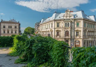 Zdjęcie przedstawiające widok na kamienicę przy skrzyżowaniu ul. 3-go Maja oraz ul. Stanisława Stojałowskiego oraz balustrade obrośniętą zielenią.  