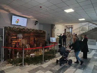Zdjęcie przedstawiające szopkę bożonarodzeniową i osoby stojące przed nią w budynku.
