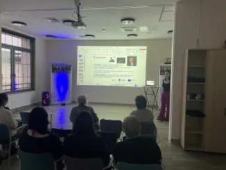 Participants during a presentation in the room – looking at a slide on the screen showing the biography of British composer Graham Fitkin.