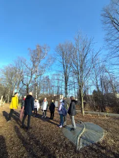 Group of people standing opposite each other with closed eyes during a mindfulness exercise led by a local musician. They are listening to the surrounding nature.