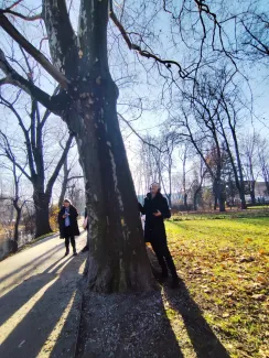 Local musician standing beside a tree with sound-recording equipment and headphones, eyes closed and smiling, listening to sounds from inside the tree.