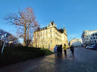 Group during a walk in the city square by the Town Hall – listening to the municipal gardener speaking while standing beside a tree decorated with Christmas ornaments.