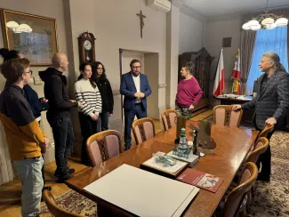 Group of people during a meeting in the Mayor’s office, standing by a table – speaking with the Deputy Mayor of Bielsko-Biała, Adam Ruśniak, and the Head of the Culture and Promotion Department of the Municipal Office in Bielsko-Biała, Przemysław Smyczek.