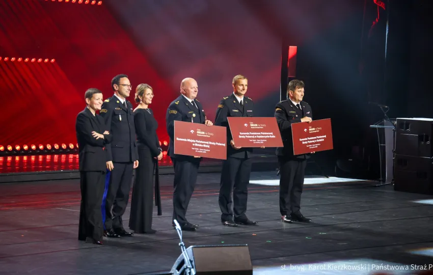 Na zdjęciu stojący ludzie 