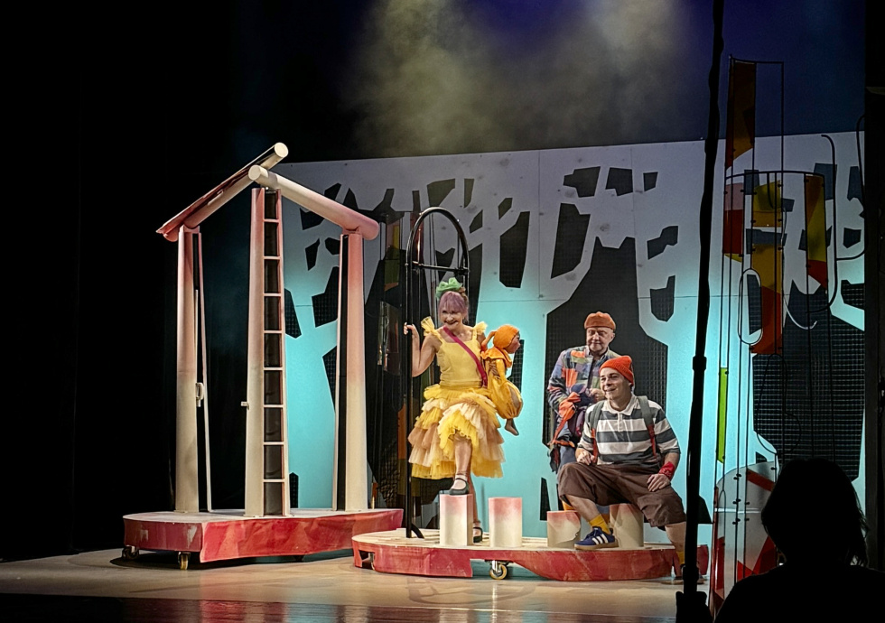 Na zdjęciu scena ze spektaklu - trzy postaci na tle scenografii