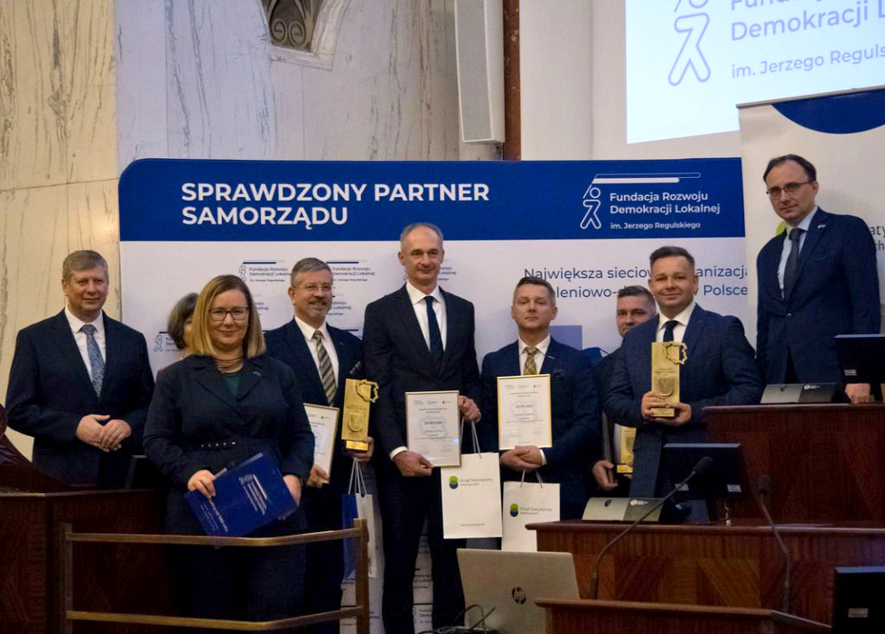 Na zdjęciu stojący ludzie 