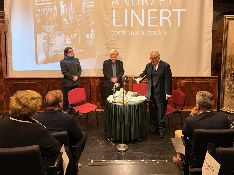 Na zdjęciu trzej panowie stoją, widoczne osoby na widowni