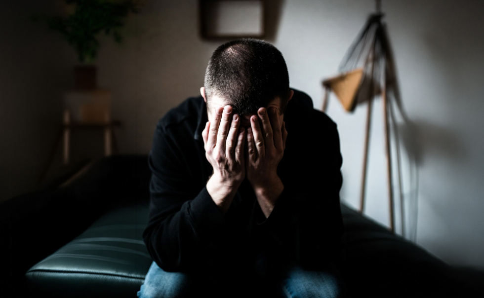 Na zdjęciu mężczyzna zakrywający twarz dłońmi