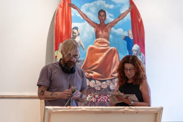 Na zdjęciu dwie osoby, za nimi obraz