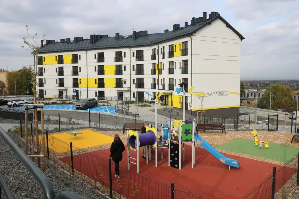 Na zdjęciu plac zabaw przed jednym z bloków, na placu widoczne osoby