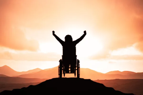 Na zdjęciu osoba na wózku na szczycie pagórka w zachodzącym słońcu 
