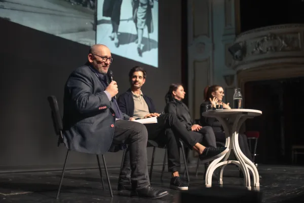 Na zdjęciu cztery osoby siedzące przy stoliku na scenie, powyżej fragment wyświetlanego zdjęcia