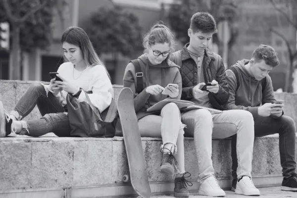 Na zdjęciu młodzież na zewnątrz, siedzi na murku z telefonami w rękach 