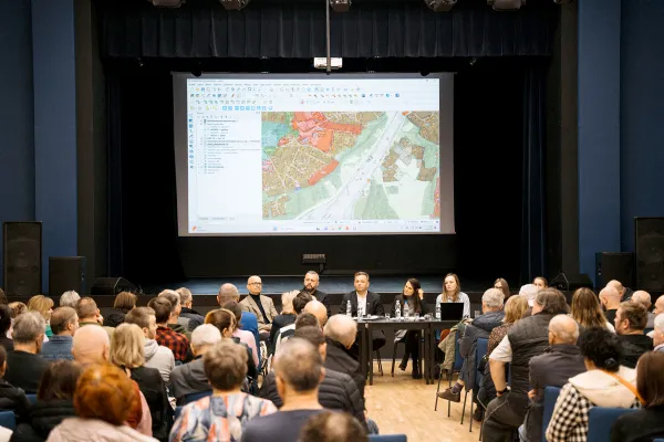 Na zdjęciu osoby na widowni i przy stole, nad nimi plansza z mapą