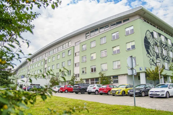 Na zdjęciu: jasnozielony, niewysoki budynek, przed nim samochody