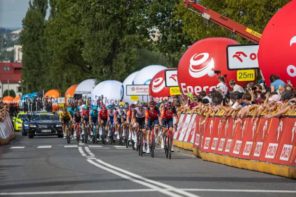 Na zdjęciu peleton kolarzy na drodze, kibice za ogrodzeniem